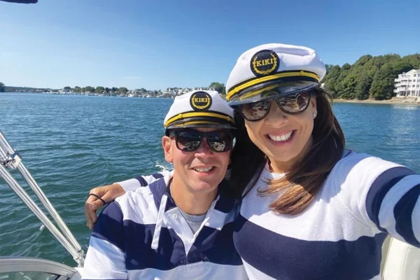 A man and a woman wearing identical clothing pose for a photo. They laugh as they embrace each other and navigate the ocean on a bright, sunny afternoon.