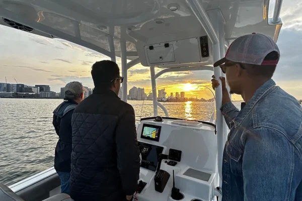 Two men and a woman are on a center console motorboat enjoying a ride in Boston Harbor as the sun rises.