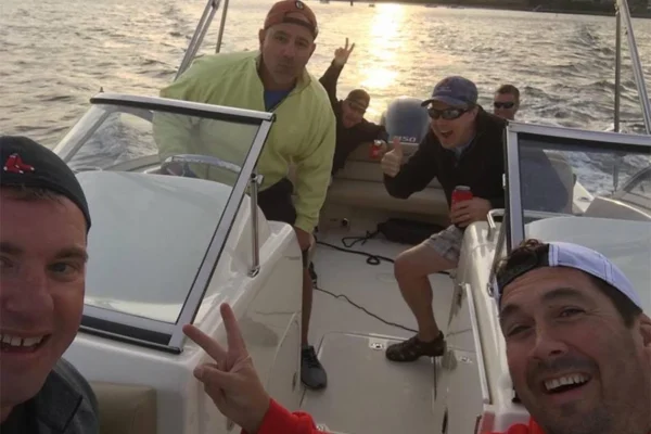 Six men enjoy a boat ride on the ocean waters while the sun rises behind them.