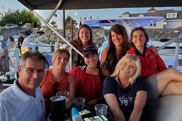 A large group of people enjoying the sunset on a boat parked in the marina.