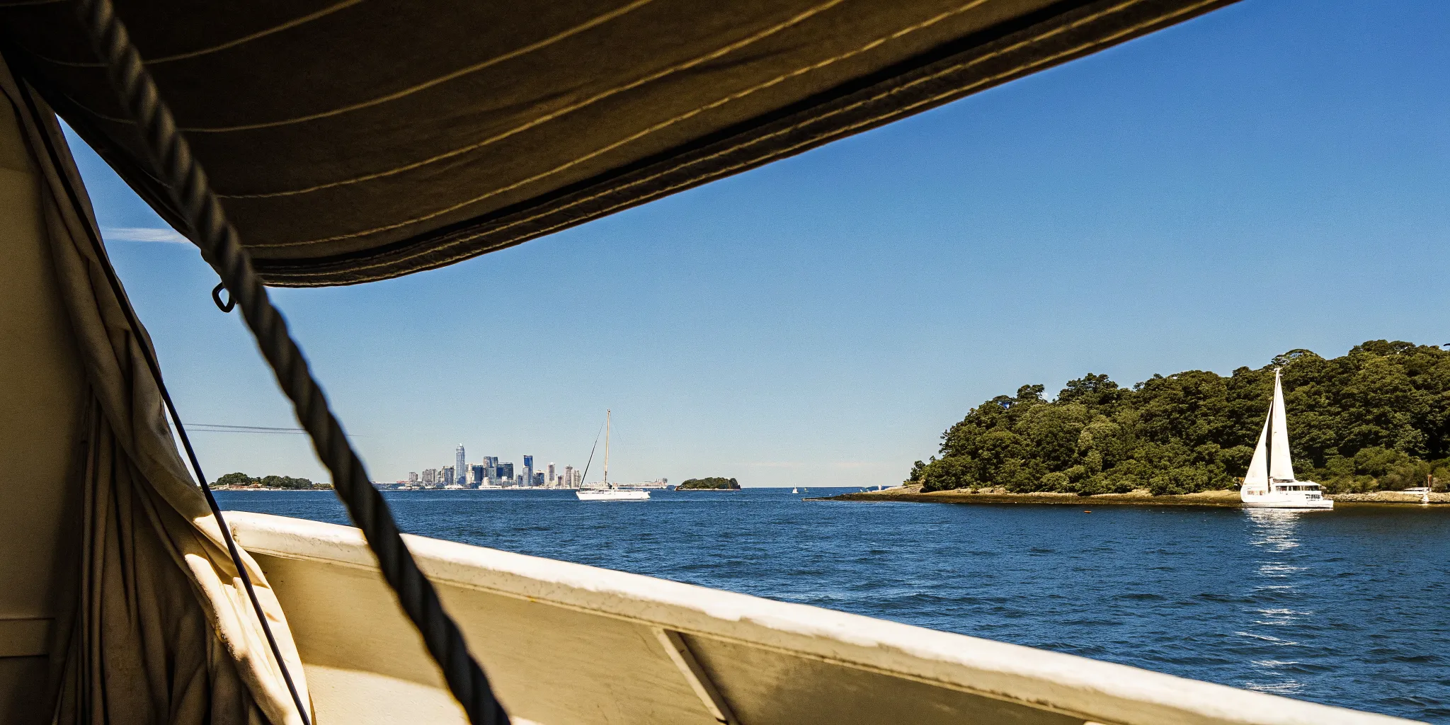 A view of Boston Harbor from a boat showing the skyline and harbor islands on a sunny day